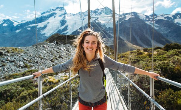 Woman on a bridge with mountains behind her.