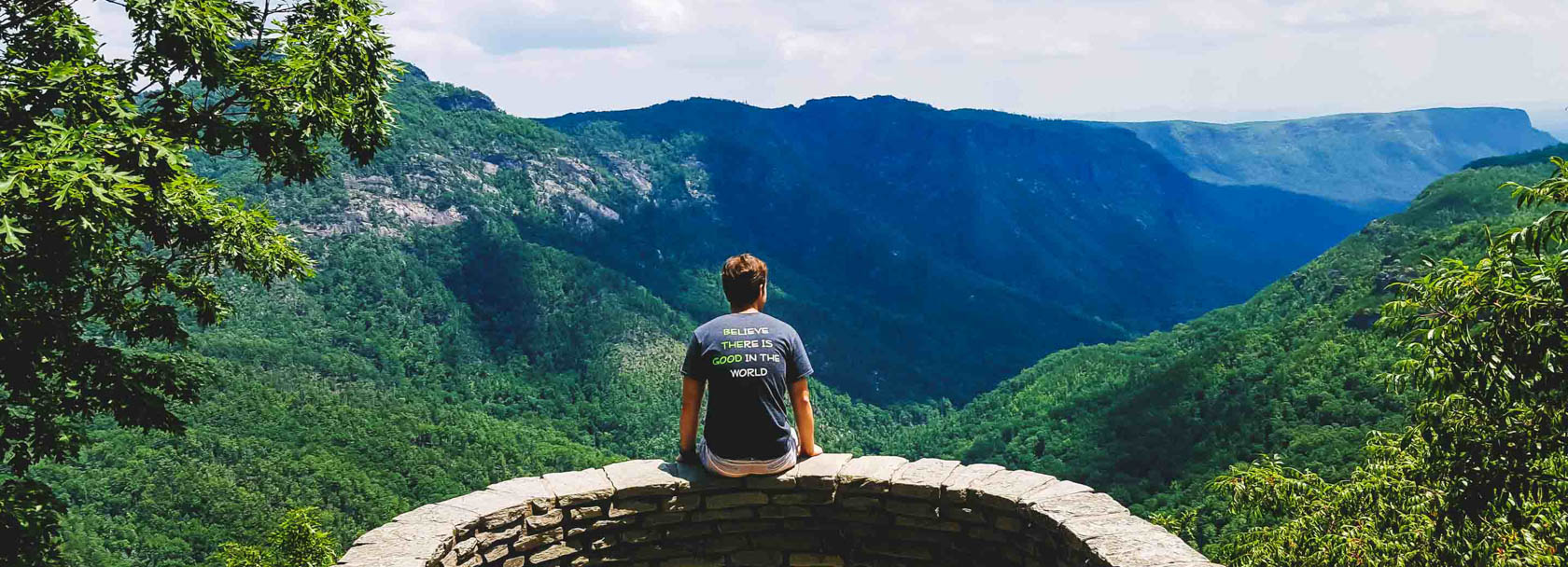 Solo traveler sitting on the edge of a wall overlooking a mountain range.