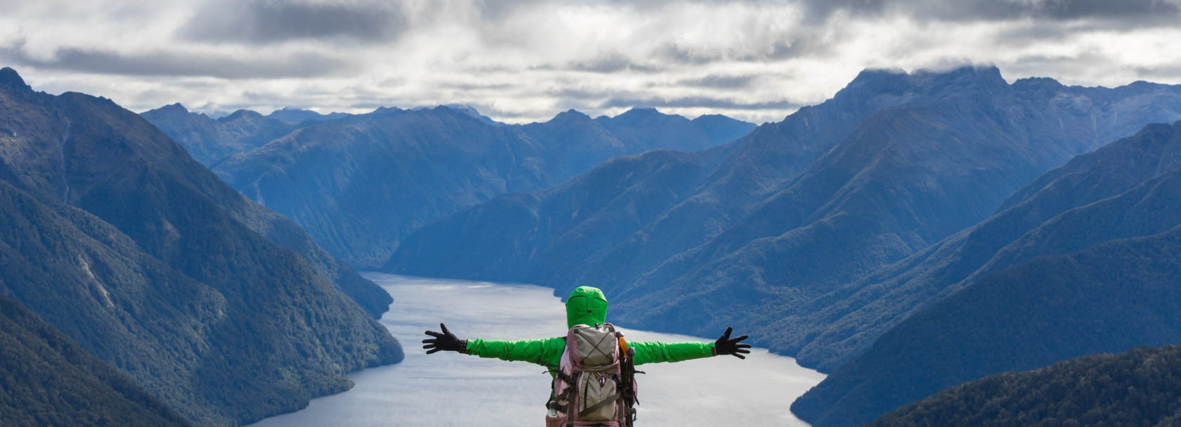 Solo traveler in New Zealand on top of a mountain with the mountain ranger in the background.