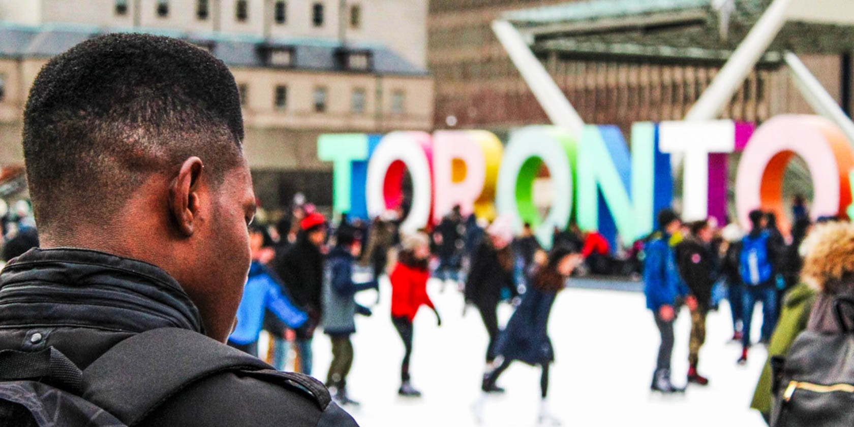 Solo traveling in front of the "Toronto" sign during the day with other tourists.